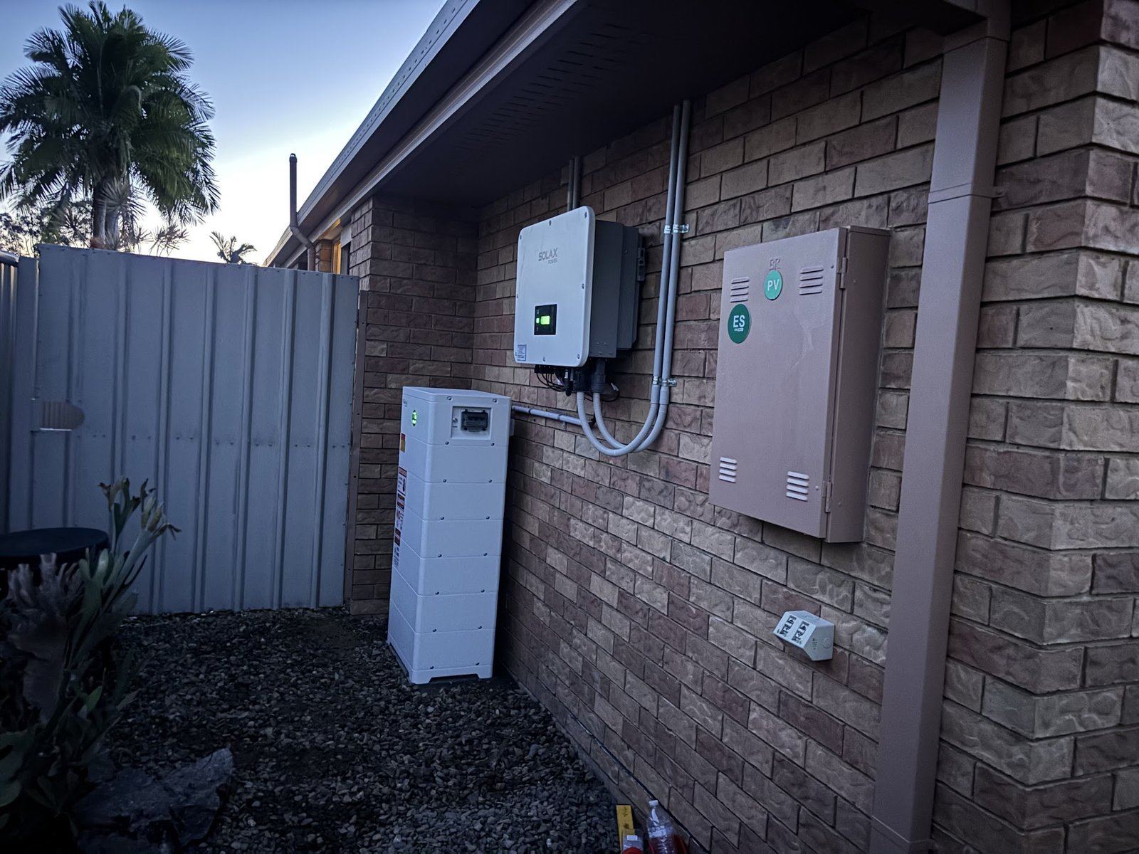 SolaX hybrid inverter and battery on a red brick wall, outdoor install