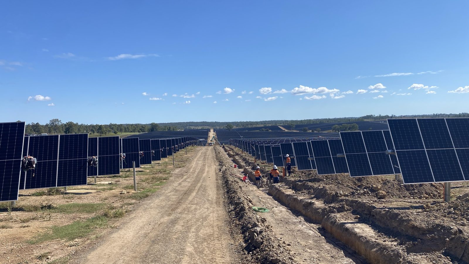 Bundaberg Solar Farm under construction — single-axis tracker rows running to the horizon, crew working the cable trench